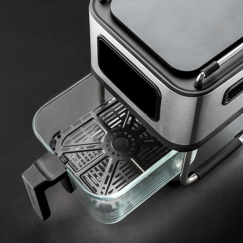 Close-up of a modern kitchen appliance with a brushed stainless steel body, black accents, and a clear glass container with a black drip tray, photographed on a dark studio background.